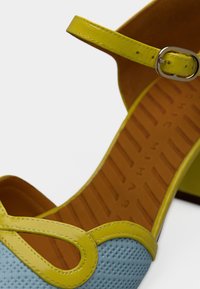 Sandale à talon bleu et jaune avec une tige texturée et une bride. Présente un design ajouré et une doublure intérieure lisse avec une semelle à motif.