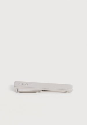 Pince à cravate en métal argenté avec le logo "HUGO" gravé sur une surface lisse et rectangulaire sur fond blanc.