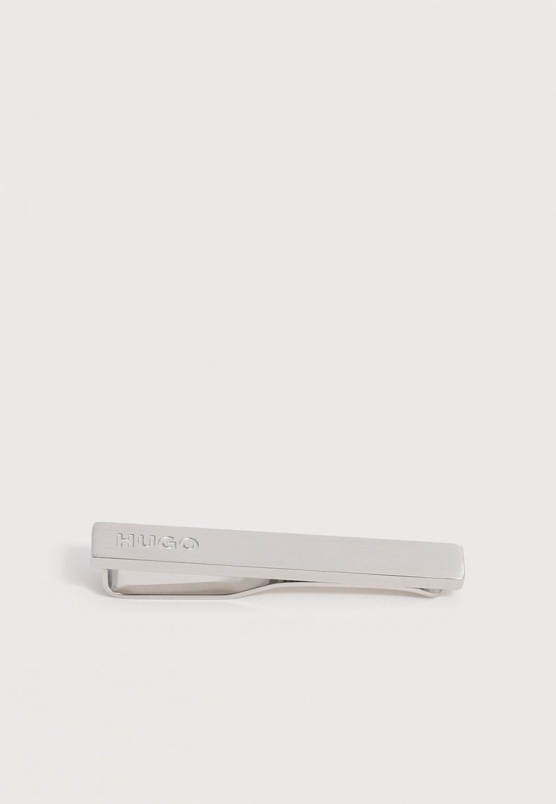 Pince à cravate en métal argenté avec le logo "HUGO" gravé sur une surface lisse et rectangulaire sur fond blanc.