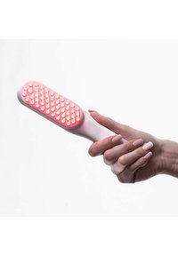 Une main tenant un appareil blanc avec une lumière LED rouge et des broches de massage en caoutchouc, sur fond blanc.