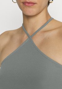 Top de malha cinza com riscas, com alças finas, apresentando um design cruzado na gola. Textura suave e forma ajustada.