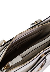 Grande borsa in pelle sintetica bianca con hardware in tonalità oro. Presenta molteplici scomparti, rifiniture nere e un rivestimento interno a contrasto.
