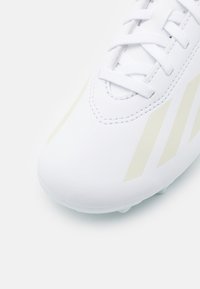 Botas de fútbol blancas con material sintético suave, punta redondeada y rayas amarillas sutiles. Los cordones están colocados en el centro para un ajuste seguro.