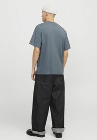 T-shirt en coton gris avec une coupe décontractée, des manches courtes et un col rond, associé à un pantalon en denim foncé avec des ourlets retournés.