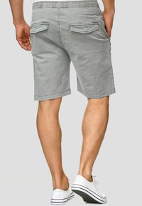 Shorts gris avec une ceinture élastique, deux poches arrière et une coupe décontractée. Le tissu semble doux avec une texture subtile. Portés avec des baskets blanches.
