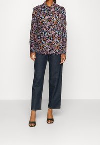 Bloemmotief blouse met donkere achtergrond, lange mouwen, kraag; gecombineerd met donkere denim wijde broek en zwarte open-tipe hakken.