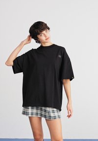 Camiseta negra de gran tamaño con mangas cortas, que presenta un pequeño parche con logo. Combinada con una falda de cuadros ligera. Diseño y textura simples.