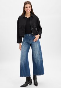 Black cropped jacket over a black top, paired with wide-leg blue jeans featuring a lighter wash and a patch pocket, complemented by black heeled boots.