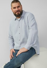 Jasnoniebieska koszula z długim rękawem w stylu button-up z teksturowanym wzorem, z guzikami na mankietach i casualowym krojem, zestawiona z dżinsami.