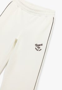 Witte joggingsbroek met elastische tailleband, voorzien van bruine zijstrepen en een geborduurd logo op de dij met de tekst "New York 1998 Social Club."