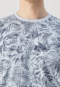 Light blue t-shirt featuring a navy palm leaf pattern. Made from soft fabric with a crew neckline and short sleeves.