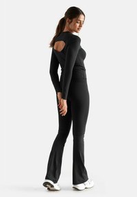 Black long-sleeve top with a cutout detail at the back, paired with flared black pants. Soft fabric and form-fitting design.