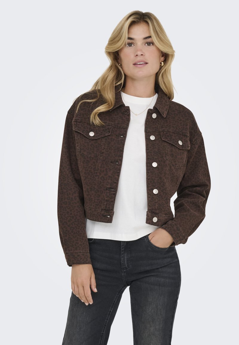 Chaqueta de mezclilla marrón con estampado de leopardo, diseño cropped, cierre frontal de botones, dos bolsillos en el pecho, llevada sobre una camisa blanca y jeans negros.