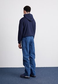 Granatowa bluza z kapturem i sznurkiem, połączona z niebieskimi spodniami cargo z wieloma kieszeniami. Stylizację dopełniają ciemne trampki.