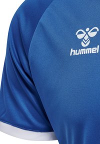 Blauwe sportshirt met een gladde textuur; heeft het Hummel-logo in het wit op de bovenste linkerkant. Korte witte rand aan de rand van de mouwen.
