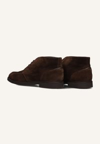 Bottines chukka en suède marron avec un bout arrondi, un laçage à l'avant et une semelle en caoutchouc lisse. Présente des accents de couture discrets et un petit talon.