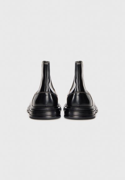 Bottes de cheville en cuir noir avec un design épuré, des côtés élastiques, des semelles en caoutchouc épaisses et des détails de couture subtils. Fini lisse et brillant.