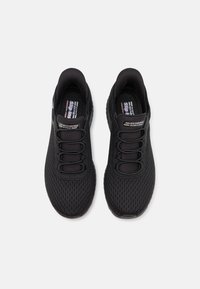 Fekete sportcipők hálós felsőrésszel, slip-on dizájnnal és fekete fűzőkkel. Jellemzője a logó részlet és a texturált gumi talp.