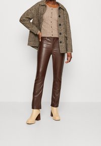 Chaqueta de patrón de espiga en marrón y beige, top de punto ligero, pantalones de cuero sintético marrón y botas de tacón grueso beige.