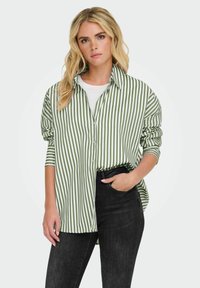Groen en wit gestreepte knoopshirt met lange mouwen, ontspannen pasvorm en een subtiele textuur, gecombineerd met donkere jeans.