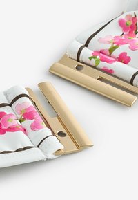 Clape de geantă din metal cu ton auriu atașate pe un material alb cu imprimeu floral roz și dungi maro pe un fundal alb.