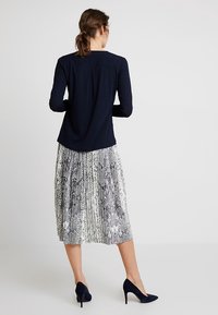 Marinblå långärmad topp i kombination med en plisserad kjol med ormskinnsmönster i svart och vitt, bärs med svarta högklackade skor.