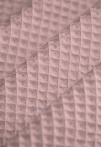 Waffelstrukturstoff in sanftem Pink mit einem Gittermuster. Das Material hat ein flauschiges Aussehen und eine leichte, atmungsaktive Qualität.