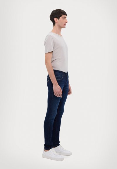 T-shirt grigio chiaro a maniche corte abbinato a jeans slim-fit blu scuro e sneakers bianche, mostrato in vista laterale.