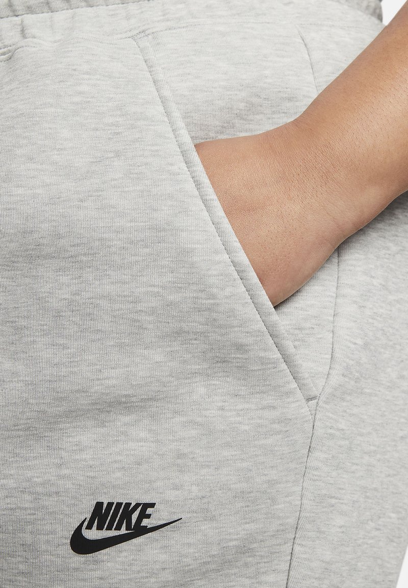 Hellgraue Jogginghosen aus weichem, strukturierter Stoff mit einer Seitentasche und einem schwarzen Nike-Logo auf dem linken Oberschenkel.