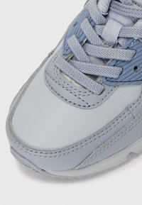Sapatilha azul clara com um cabedal em couro liso, detalhes texturizados, atacadores planos e costura reforçada nas bordas.