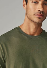 Olivgrünes Kurzarm-T-Shirt mit Rundhalsausschnitt, aus weichem Stoff gefertigt, mit glatter Textur und sauberer Naht entlang des Ausschnitts.