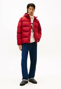 Rød puffjakke med hætte, prydet med quiltede sektioner. Bæres over en hvid sweater, parret med mørkeblå jeans og sorte loafers.