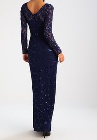 Marinblå spetsklänning för kvällsevenemang med långa ärmar, V-kärlsrygg och paljettdekorationer genom hela, figurnära silhuett ner till golvet.
