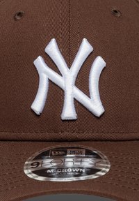 Καφέ μπέιζμπολ καπέλο με λευκό κεντημένο λογότυπο NY στο μπροστινό μέρος, με στρογγυλή αυτοκόλλητη ετικέτα New Era στο γείσο. Ρυθμιζόμενο μέγεθος.