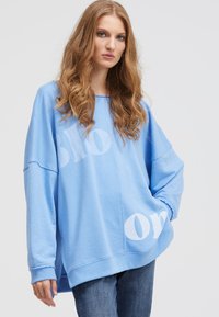 Light blue oversized sweatshirt with a crew neckline, featuring white graphic text. Made from soft fabric with ribbed cuffs and hem.