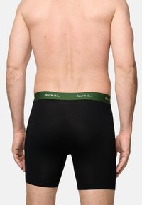 Schwarze Baumwoll-Boxershorts mit einem grünen elastischen Bund, der weiße Schriftzüge trägt. Entworfen für Komfort und eine eng anliegende Passform.