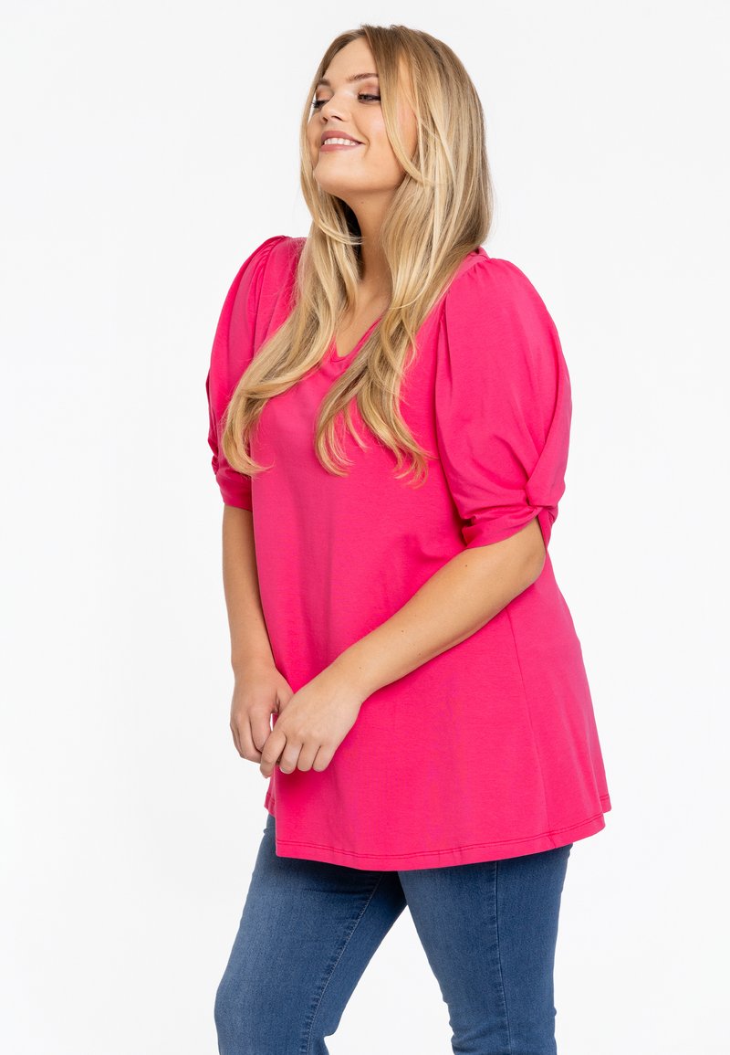 Roze top met pofmouwen, gemaakt van zachte stof, met een ronde halslijn en een ontspannen pasvorm, gecombineerd met blauwe skinny jeans.