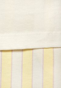 Baumwollmischgewebe mit einem cremfarbenen oberen Abschnitt. Darunter ein gestreiftes Muster in Gelb und Hellrosa. Sichtbare Nähte an der Naht.