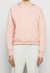 Rosa hoodie i mjukt material med en kanguroficka, ribbad manschett och nederkant. Har en liten logotyp ovanför bröstet och en huva med dragsko.