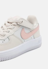 Bež Nike tenisice s ružičastim detaljima, od kože i tekstila, s округлим vrhom, ravnim bijelim đonom i teksturiranim vezicama.
