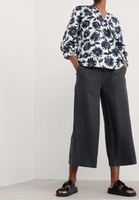 Witte blouse met marineblauwe bloemenprint, driekwart mouwen, gecombineerd met donkergrijze wijde broek en zwarte instapsandalen.