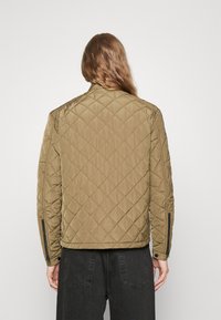 Giacca bomber trapuntata in verde oliva, con colletto alto, tasche laterali con zip e polsini a costine con una texture liscia.