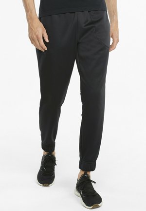 Schwarze Sport-Jogginghosen mit elastischen Bündchen und Seitentaschen, aus einem glatten, leichten Stoff gefertigt. Tragen mit schwarzen Sportschuhen.