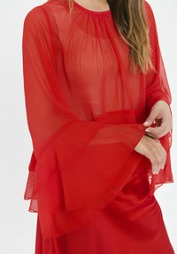 Rote, transparente, mehrlagige Bluse mit langen, ausgestellten Ärmeln und rundem Ausschnitt. Sanfte Textur mit fließender Silhouette.