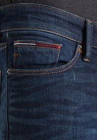 Mörkblå denimjeans med tydlig sömnad, en liten bakficka med röd och vit accenttråd och en klassisk passform.