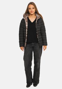 Doudoune noire avec doublure imprimé léopard, dotée d'une fermeture éclair à l'avant, d'un design matelassé et d'une capuche. Portée par-dessus un haut noir à col en V et un jean foncé.