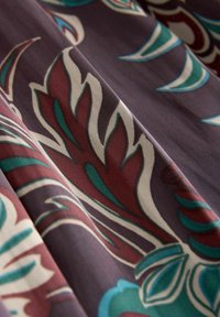 Látka s květinovým vzorem v barvách burgundské červené, modrozelené a krémové na tmavě fialovém pozadí, vyznačující se hladkou texturou a složitým designem.