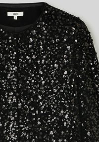Veste en velours noir ornée de paillettes argentées, dotée d'un col rond et d'un design simple, mettant en valeur des textures brillantes et une coupe ajustée.