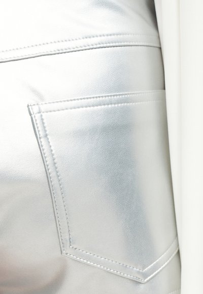 Κοντινή λήψη ενός λεία, γυαλιστερού ασημένιου δερμάτινου ενδύματος με ραμμένη πίσω τσέπη και λεπτομερείς γραμμές ραφής.