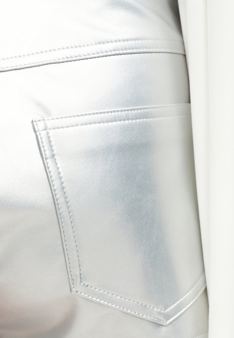 Gros plan sur un vêtement en cuir argenté lisse et brillant avec une poche arrière cousue et des lignes de couture détaillées.